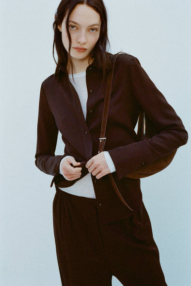 Image of model wearing Maddi Shirt in Merino Wool Twill in Chocolate over a white shirt against a light blue background