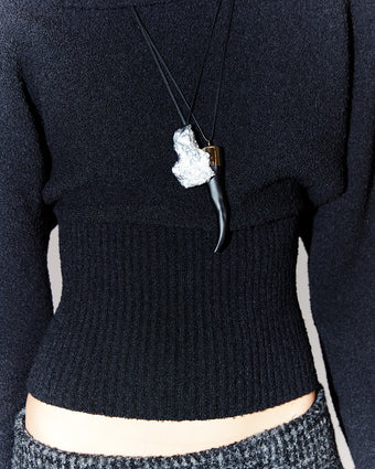 close crop of a black sweater with a silver necklace and a top of a pair of trousers showing at the bottom of the image