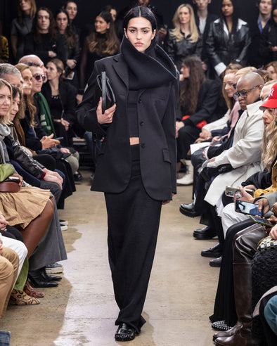 Model Walking in Proenza Schouler Fall Winter 2024 Runway Show Wearing Archer Jacket in Black Wool Twill , Alyssa Sweater in Charcoal Wool Viscose Knit, Avalon Skirt in Black Lacquered Knit, Tube Scarf in Black Cashmere Knit, City Bag in Black Nappa, and Park Loafers in Black Slick Nappa