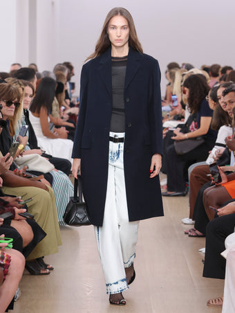 Model walking Proenza Schouler SS24 Runway in Kiki Tank In White Cotton Mesh, Dara Top In Black Technical Nylon Jersey, Ellsworth Jean In Bleached Denim, Silva Coat In Navy Brushed Cotton Suiting, Park Shoulder Bag In Black Nappa Leather, Tee Toe Ring Sandals In Black + Cream Nappa Lux