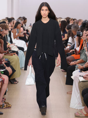 Model Walking Proenza Schouler SS24 Runway In Amy Sweater In Black Viscose Boucle, Joey Pant In Navy Brushed Cotton Suiting, Park Shoulder Bag In Optic White Nappa Leather, Monogram Loafers In Black Nappa