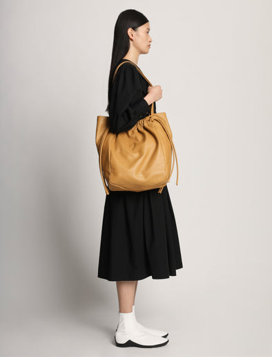 Image of model carrying Drawstring Tote in CARAMEL