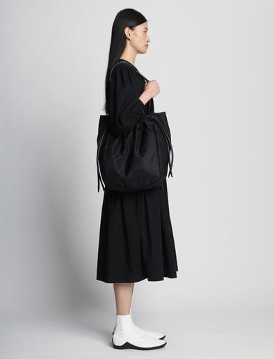 Side image of model carrying Nylon Drawstring Tote in BLACK on shoulder