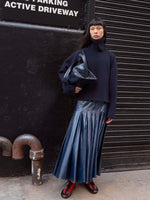 Image of model standing on the sidewalk wearing the Petra Skirt in Lacquered Cotton in Navy and the Arcadia Sneakers in Red holding the Days Carryall Bag in Navy
