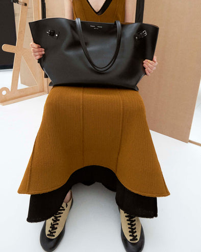 Cropped image of model sitting holding the a bag wearing the Tavia Dress in Viscose Fringe Knit in Olive and the Arcadia Sneakers in Almond holding the Days Carryall in Smooth Calf in Black