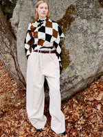 Model standing against stone boulder wearing Vanne Top in Light Green Argyle Velvet Knit, Salome Pant in Ecru Corduroy, Braid Belt in Bordeaux Croc Embossed Calf, and Uma Ankle Boots in Black Silk Calf