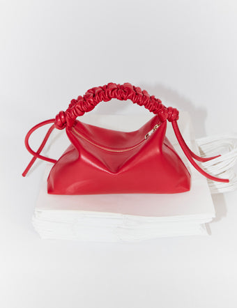 Mini Drawstring Bag in new scarlet on stack of white paper bags