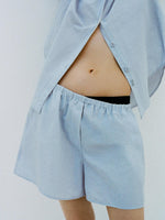 Cropped image of a model leaning against a white backdrop, wearing Caroline Shirt in Linen Shirting and Jana Short in Linen Shirting in Light Oxford Melange