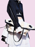 Cropped image of model standing against pink backdrop, wearing Laci Skirt in Eco Cotton Poplin in White holding Days Carryall in Striped Canvas in Resin/White