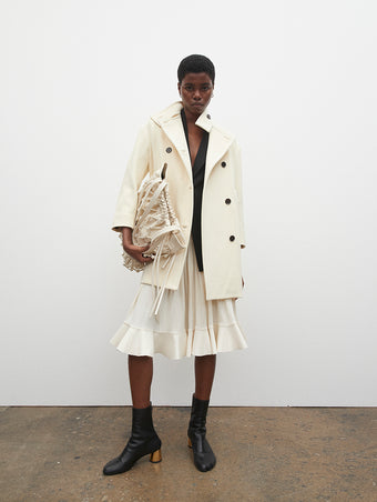 PF23 Collection Look 01: Ecru Technical Gabardine Peacoat, Black Viscose Suiting Jacket, Ivory Crepe Jersey Skirt, Ecru Macrame Drawstring Tote, and Black Sculpt Ankle Boots with Gold Heel