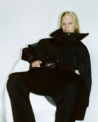 Image of Pamela Anderson in Maxwell Anorak in Nylon Gaberdine in black, sitting in white chair
