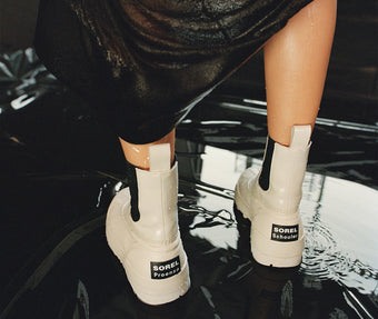 Image of model standing in puddle wearing SOREL x Proenza Schouler Caribou Chelsea Boots in chalk black