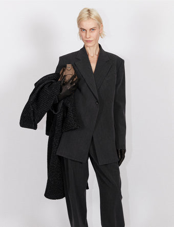 Model in Melange Wool Jacket and Trousers in grey holding Beacon Saddle Bag in mushroom
