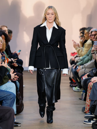 Chloe Sevigny in Black Wool Felt Jacket, White Crushed Matte Satin Shirt, Black Nappa Leather Skirt, Black Cone Over The Knee Boots, and Black Smooth Nappa Strobel Belt