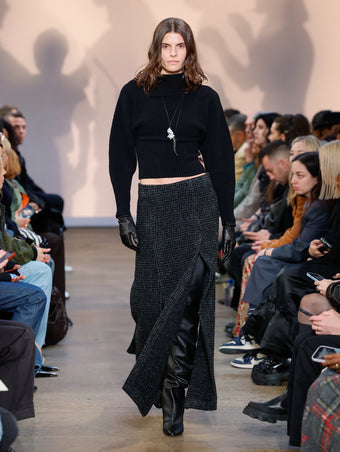 Model in Black Viscose Boucle Sweater, Charcoal Melange Wool Boucle Skirt, Black Cone Over The Knee Boots, Black/gold Horn Pendant Necklace, Silver Rock Pendant Necklace, and Black Leather Gloves