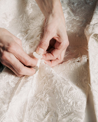 4x5 image of hands sewing a button on Chrysanthemum Jacquard fabric