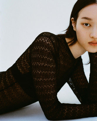 Focus cropped image of model laying down on a white backdrop wearing the Miriam Dress in Crochet in Black