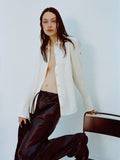 Image of model wearing Maddi Shirt in Merino Wool Twill in Bone and Magnus Pants in Lightweight Leather in Black holding onto a chair against a plain background