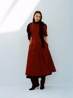 Model wearing Ainsley Dress in Tech Cotton in Claret with a black scarf on shoulders against a white background