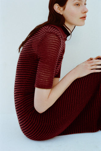Image of model wearing Meline Dress in Cashmere Silk Stripe in Claret, black on a light blue background