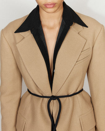 close crop of a tan coat with a black button down underneath and a black slim belt
