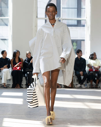 Image of model walking Proenza Schouler SS25 Runway wearing Isla Dress in Stripe Cotton Silk Poplin in  Navy Multi and Days Carryall in Off-White Smooth Calf in OFF-WHITE and Tee Feather Thong Sandal in RESIN