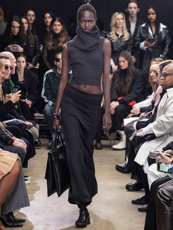 Model walking in Proenza Schouler Fall Winter 2024 Runway show wearing CRUZ SWEATER IN CHARCOAL WOOL VISCOSE KNIT, AVALON SKIRT IN BLACK LACQUERED KNIT, TUBE SCARF IN CHARCOAL WOOL VISCOSE KNIT, Split Tote in Black Nappa, Silo Bag in Black Nappa,  and TRACK SNEAKERS IN BLACK NAPPA/SUEDE