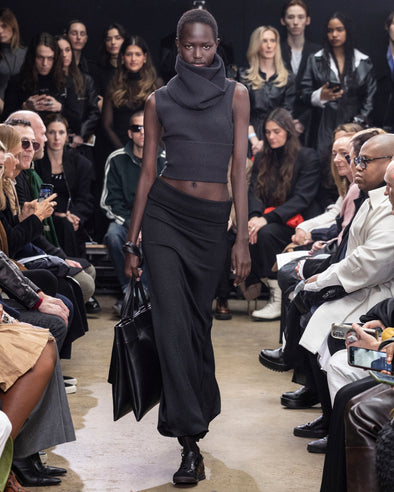 Model Walking In Proenza Schouler Fall Winter 2024 Runway Show Wearing Cruz Sweater In Charcoal Wool Viscose Knit, Avalon Skirt In Black Lacquered Knit, Tube Scarf In Charcoal Wool Viscose Knit, Split Tote In Black Nappa, Silo Bag In Black Na