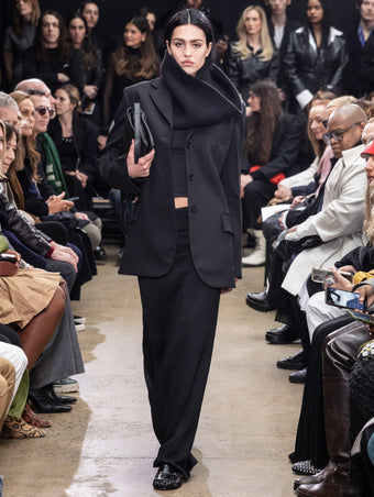 Model Walking in Proenza Schouler Fall Winter 2024 Runway Show Wearing Archer Jacket in Black Wool Twill , Alyssa Sweater in Charcoal Wool Viscose  Knit, Avalon Skirt in Black Lacquered Knit, Tube Scarf in Black Cashmere Knit, City Bag in Black Nappa, and Park Loafers in Black Slick Nappa