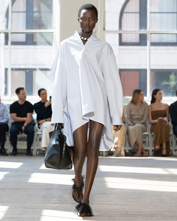 Image of model walking Proenza Schouler SS25 Runway wearing Isla Dress in Stripe Cotton Silk Poplin in Pale Blue Multi and Days Carryall in Black Smooth Calf in BLACK and Tee Feather Thong Sandal in BLACK