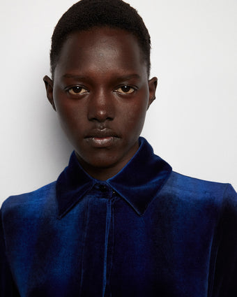 close cropped image of a model wearing blue velvet button down dress, looking directly into the camera against a white background