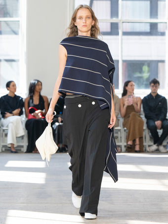 Image of model walking Proenza Schouler SS25 Runway wearing Sutton Top in Stripe Bi-Stretch Viscose in Navy Multi and Oliver Pant in Wool Gabardine in Black and Tee Ankle Boots in Optic White
