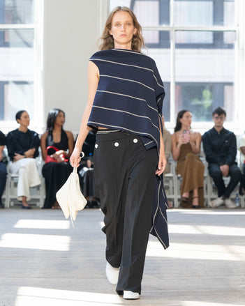 Image of model walking Proenza Schouler SS25 Runway wearing Sutton Top in Stripe Bi-Stretch Viscose in Navy Multi and Oliver Pant in Wool Gabardine in Black and Tee Ankle Boots in Optic White