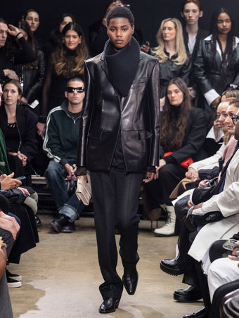 Model Walking in Proenza Schouler Fall Winter 2024 Runway Show Wearing Hayes Jacket in Black Leather, Rio Top in Black Tulle Jersey, Chase Pant in Black Technical Mesh Suiting, Tube Scarf in Black Cashmere Knit, Flip Shoulder Bag in Taupe Eel, and  Bronco Chelsea Boots in Black Box Calf