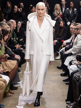 Model Walking in Proenza Schouler Fall Winter 2024 Runway Show Wearing Reed Coat in Ecru Eco Double Face Wool, Split Tote in Cream Nappa, Silo Bag in Cream Embossed Ostrich Calf, and  Monogram Loafers in Black Shiny Eel