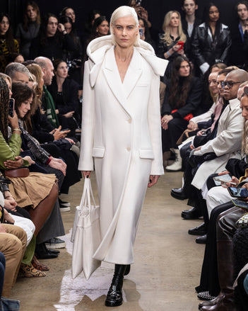Model Walking in Proenza Schouler Fall Winter 2024 Runway Show Wearing Reed Coat in Ecru Eco Double Face Wool, Split Tote in Cream Nappa, Silo Bag in Cream Embossed Ostrich Calf, and  Monogram Loafers in Black Shiny Eel