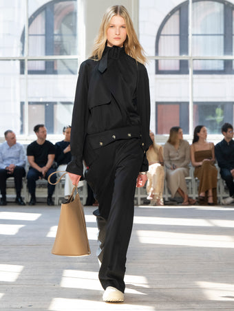 Image of model walking Proenza Schouler SS25 Runway wearing Adrien Jacket in Fluid Viscose in Black and Emmeline Shirt in Printed Silk Viscose in Sand Multi and Darya Pant in Fluid Viscose in Black and Brant Bucket Bag in Cumin Smooth Calf in CUMIN and Chelsea Boot in Chalk