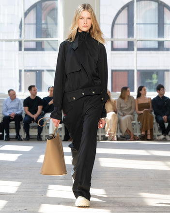 Image of model walking Proenza Schouler SS25 Runway wearing Adrien Jacket in Fluid Viscose in Black and Emmeline Shirt in Printed Silk Viscose in Sand Multi and Darya Pant in Fluid Viscose in Black and Brant Bucket Bag in Cumin Smooth Calf in CUMIN and Chelsea Boot in Chalk