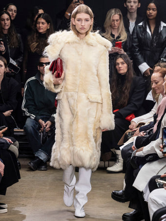 Model Walking in Proenza Schouler Fall Winter 2024 Runway Show Wearing Fiona Coat in Resin Sheared Toscana, City Bag in Rosewood Eel, and Tee Knee High Boots in White Nappa
