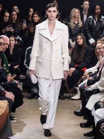 Model Walking in Proenza Schouler Fall Winter 2024 Runway Show Wearing Rowen Peacoat in Ecru Eco Double Face Wool, Teddy Pant in Bone Viscose Twill, Silo Bag in Optic White Knotted Nappa, and  Track Sneakers in Black Nappa/nylon/suede
