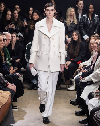 Model Walking in Proenza Schouler Fall Winter 2024 Runway Show Wearing Rowen Peacoat in Ecru Eco Double Face Wool, Teddy Pant in Bone Viscose Twill, Silo Bag in Optic White Knotted Nappa, and  Track Sneakers in Black Nappa/nylon/suede
