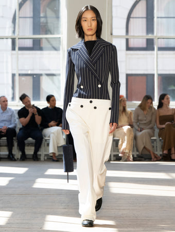 Image of model walking Proenza Schouler SS25 Runway wearing Marine Jacket in Bi-Stretch Viscose in Navy Multi and Prescott Top in Matte Viscose Crepe in Black and Oliver Pant in Wool Gabardine in Off White and Silo Bag in Deep Navy Kid Suede in DEEP NAVY and Mini Monogram Loafer in BLACK