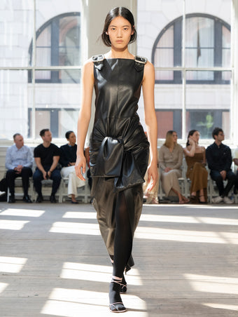 Image of model walking Proenza Schouler SS25 Runway wearing Jackie Dress in Nappa in Black and Slash Tie Sandal in LILAC