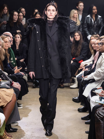 Model Walking in Proenza Schouler Fall Winter 2024 Runway Show Wearing Wilder Coat in Black Technical Nylon, Archer Jacket in Black Wool Twill , Rio Top in Black Tulle Jersey, Teddy Pant in Black Wool Twill, Flip Shoulder Bag in Black Eel, and Chelsea  Bronco Ankle Boots in Black Brushed Calf