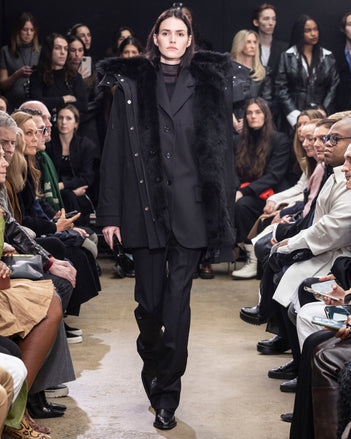 Model Walking in Proenza Schouler Fall Winter 2024 Runway Show Wearing Wilder Coat in Black Technical Nylon, Archer Jacket in Black Wool Twill , Rio Top in Black Tulle Jersey, Teddy Pant in Black Wool Twill, Flip Shoulder Bag in Black Eel, and Chelsea  Bronco Ankle Boots in Black Brushed Calf