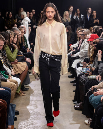 Model Walking in Proenza Schouler Fall Winter 2024 Runway Show Wearing Smithson Shirt in Resin Silk Knit, Ryman Jean in Black Garment Printed Denim, Crush Clutch in Silver Metal, Thin Belt in Black Nappa, and Tee Over the Knee Boots in Vermillion Viscose Knit