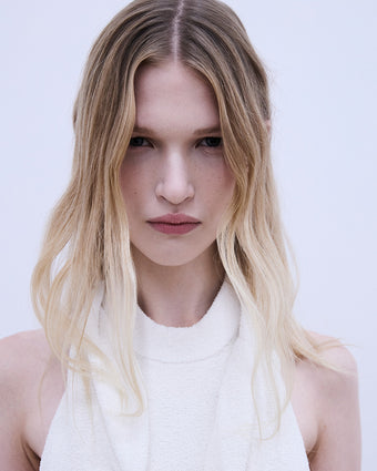 image of a model looking at the camera with blonde hair falling in her face wearing a white dress from SS24 Collection