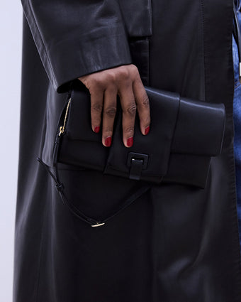 image of a model holding a black satin bag with red nail polish against a black leather jacket