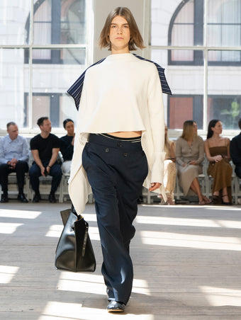 Image of model walking Proenza Schouler SS25 Runway wearing Terese Sweater in Wool Cashmere in Off White and Oliver Pant in Technical Nylon Jacquard in Midnight and Days Carryall in Black Smooth Calf in BLACK and Glove Shoe in BLACK