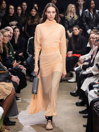 Model Walking in Proenza Schouler Fall Winter 2024 Runway Show Wearing Paula Dress in Blush Sheer Crepe Jersey, Stiltsman Stirrup in Black Compact Jersey, Silo Bag in Grey Embossed Ostrich Calf, and Tee Toe Ring Sandal in Black Nappa